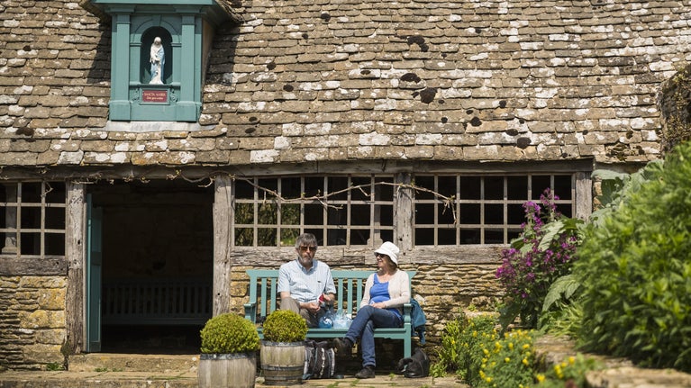 Visitors sat on a bench outside the Sancta Maria Byre at Snowshill Manor and Garden, Gloucestershire